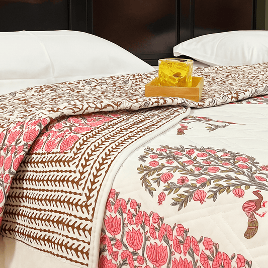 Jaipuri handprinted quilt with pink and brown floral border and reversible vine print, styled with wooden tray and yellow drink