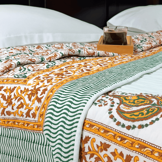 Close-up of floral paisley quilt with striped green border and orange detailing, folded neatly with a glass tray placed on top.