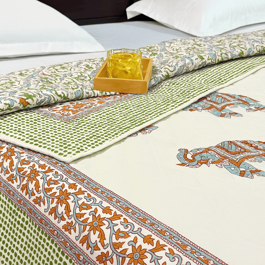 Close-up of traditional elephant block print quilt with green dotted border, styled with a rolled edge and yellow glass on tray.