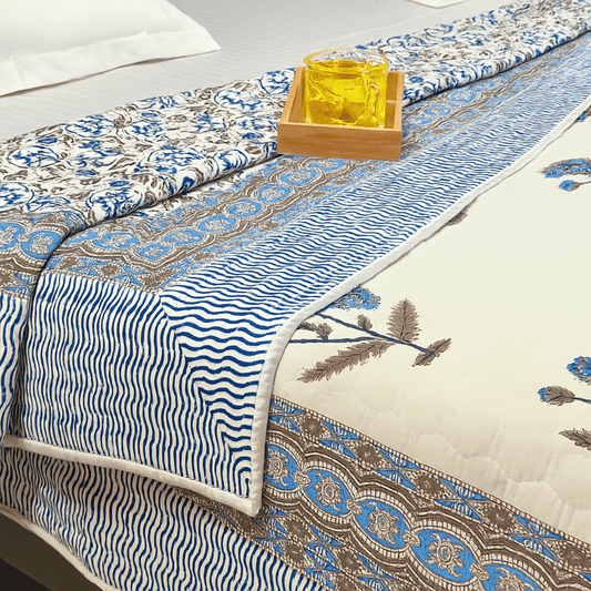 Close-up of Jaipuri quilt showcasing blue floral motifs, wavy striped border, and elegant layering with a yellow drink tray on top.