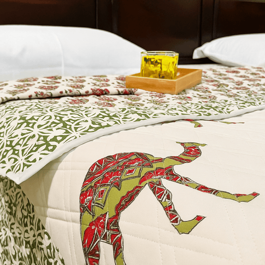 Close-up of handprinted camel quilt with intricate red and green detailing, topped with a yellow glass on wooden tray