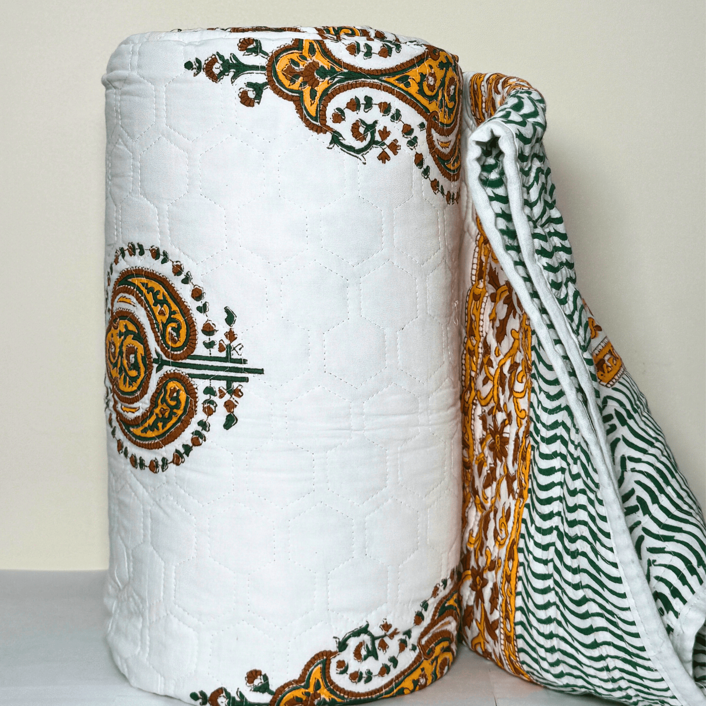 Rolled Jaipuri quilt with detailed paisley block prints and floral borders, showing both the printed front and striped reverse side.