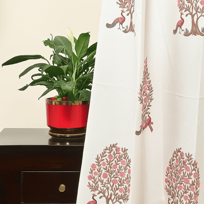 Cotton curtain with pink peacock and pomegranate tree print, styled beside red planter with green indoor plant