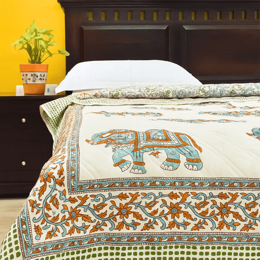 Handprinted cotton quilt with turquoise elephant motifs and floral borders, neatly spread on a bed with a wooden headboard.