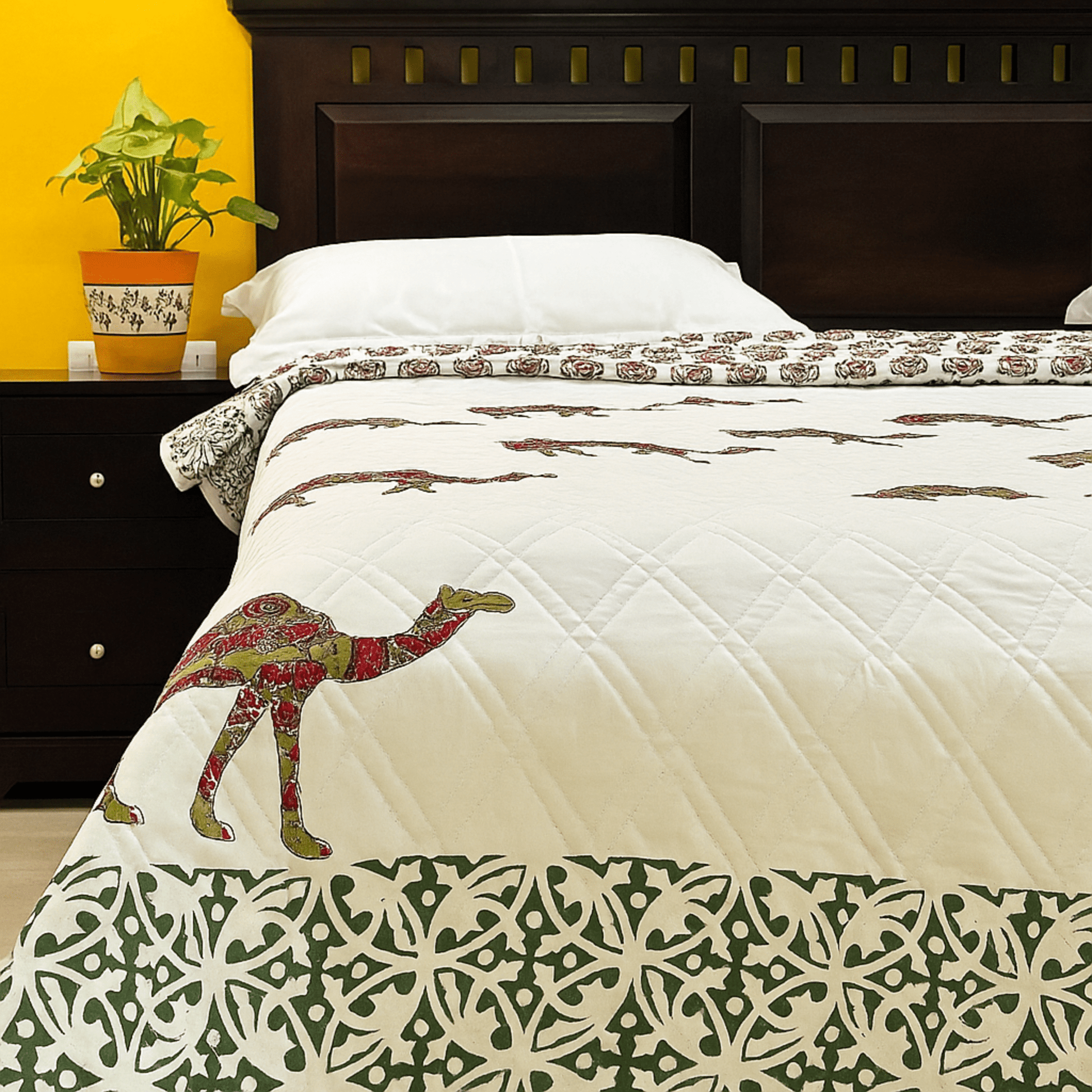 Handprinted cotton quilt with camel motif and green border, styled on a bed with white pillows and wooden headboard.