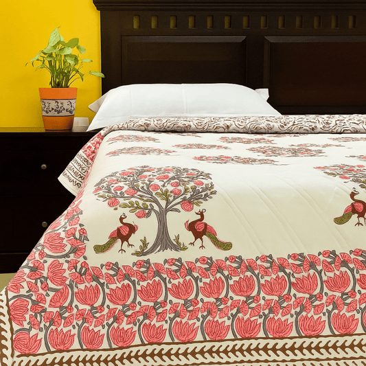 Cotton quilt with pink peacock and pomegranate tree block print, styled on a bed with white pillows and yellow background
