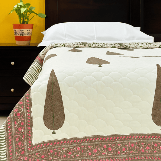 Handprinted cotton quilt with cypress tree block print and floral border, styled on bed with white pillows