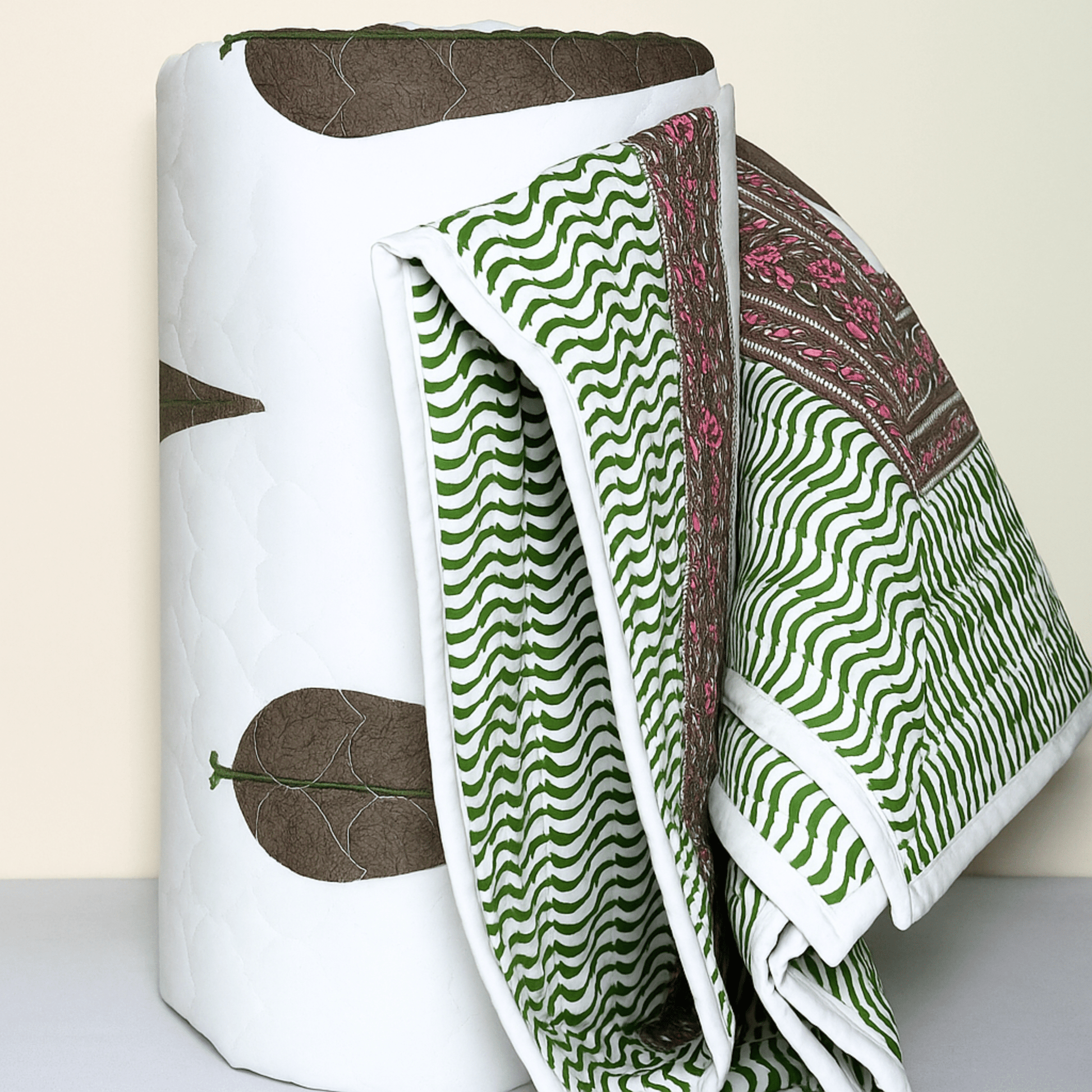 Rolled cotton quilt showing wave-patterned green print and floral edge with brown tree motif