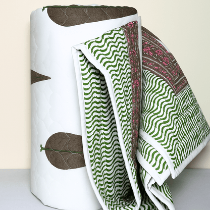 Rolled cotton quilt showing wave-patterned green print and floral edge with brown tree motif