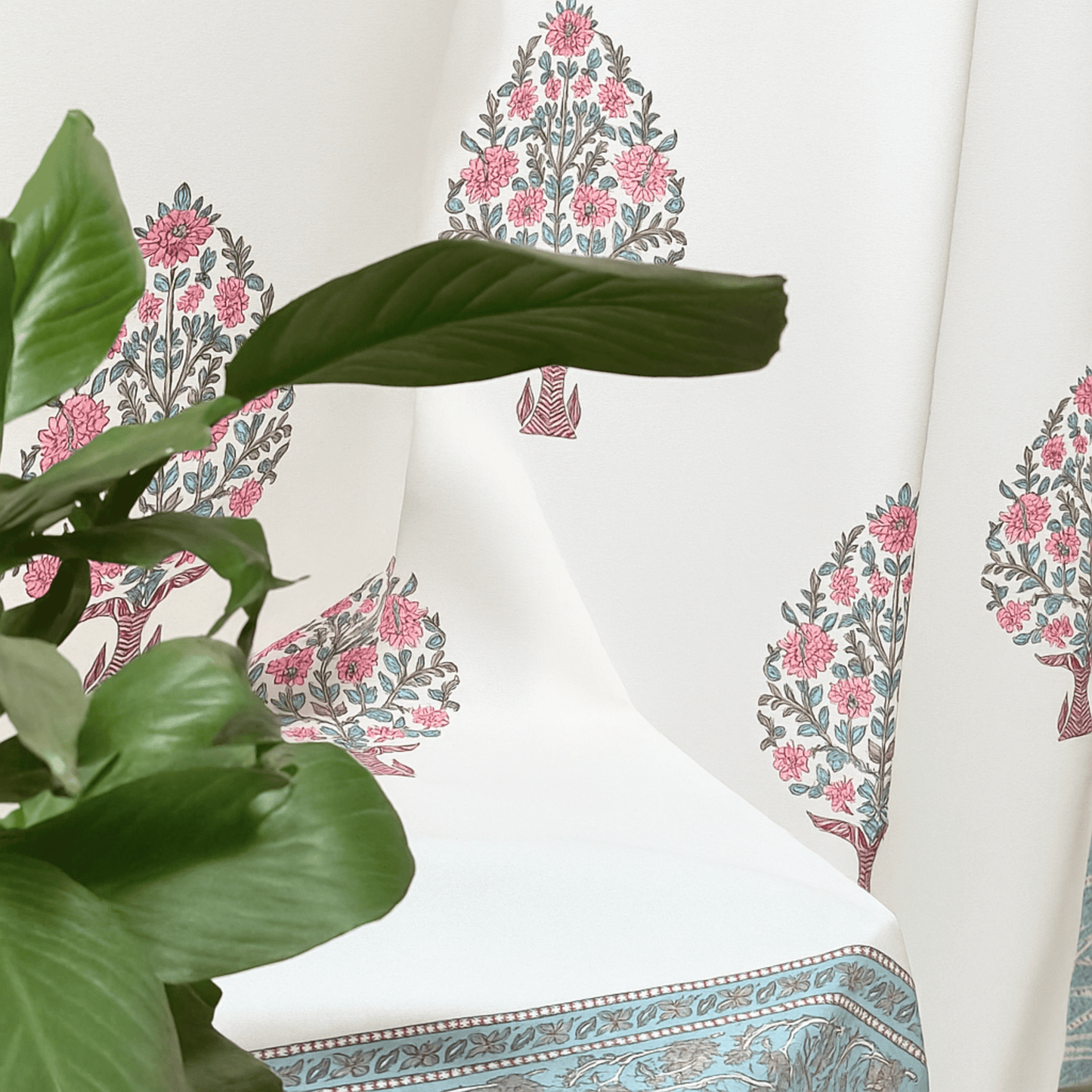 Aesthetic side view of cotton curtain with pink floral tree block print, styled with a green indoor plant in the foreground

