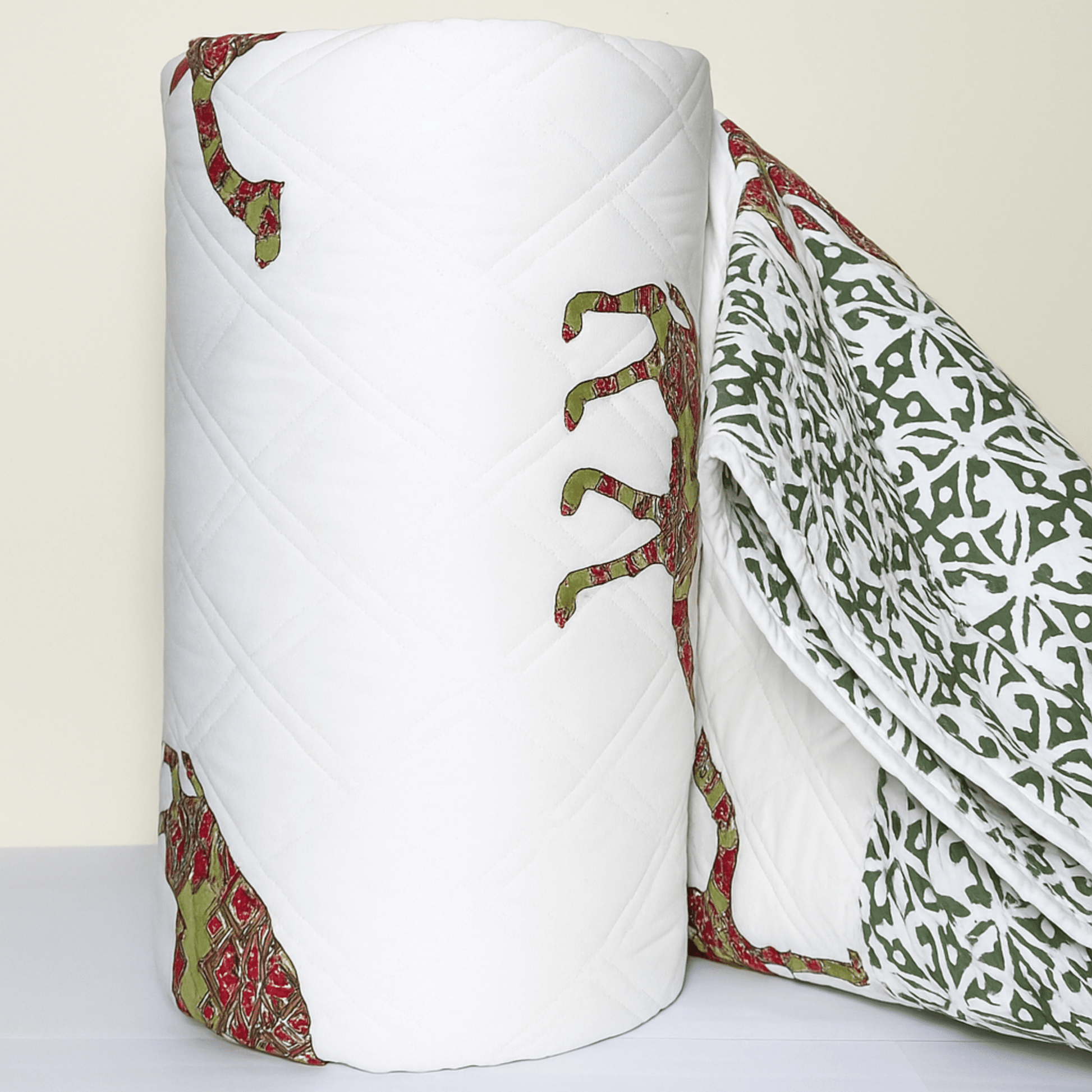 Rolled cotton quilt with traditional camel block print in red and green, showcasing fine quilting and border design.