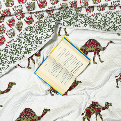 Flat lay of quilt with camels and palatial motifs, featuring a green printed border and an open book resting on the fabric.