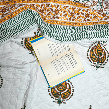 Flat lay of paisley handprinted quilt with wavy green borders and a book placed casually for a cozy reading setting.
