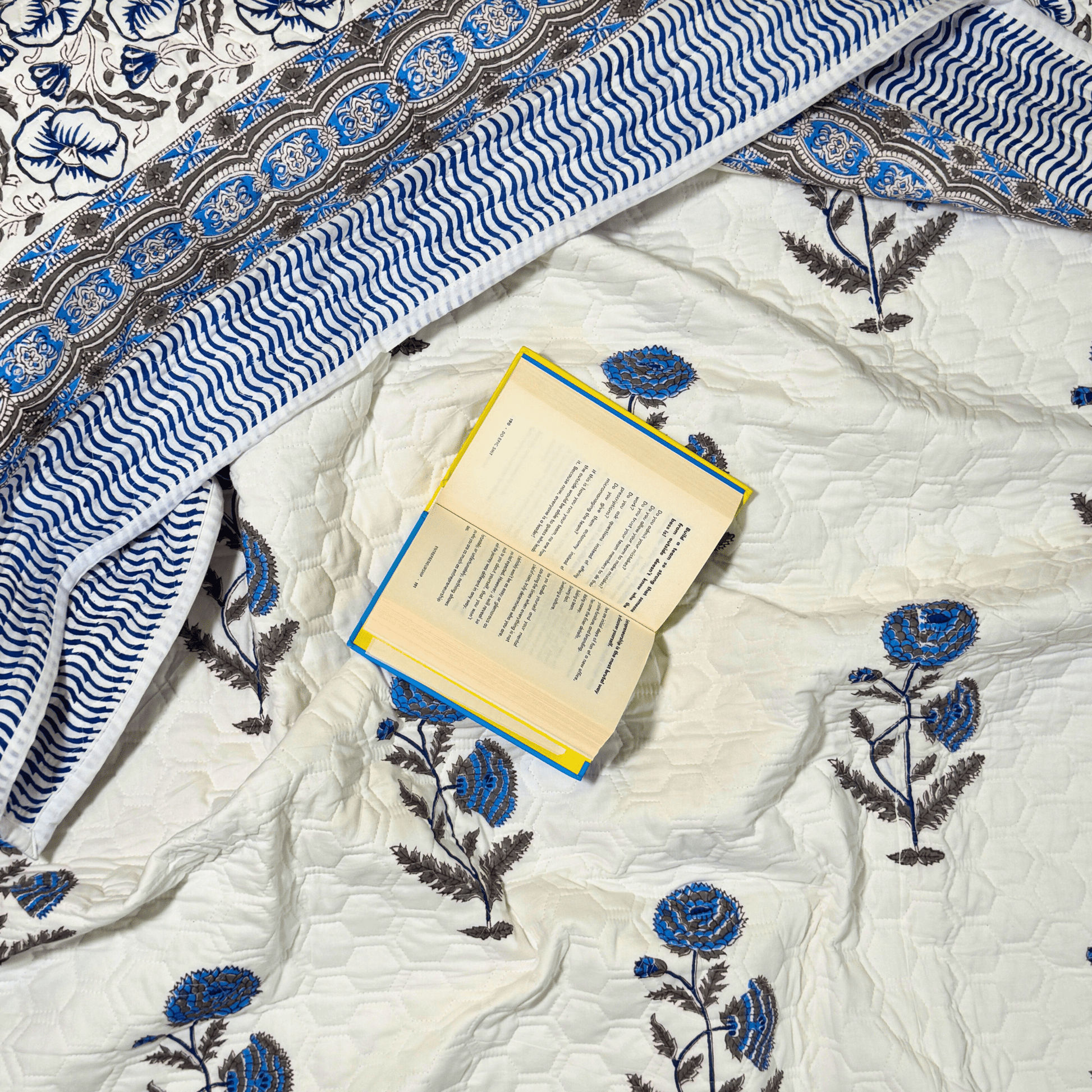 Flat lay of floral quilt in shades of blue and brown with a honeycomb stitched base and a book placed open for a cozy look.