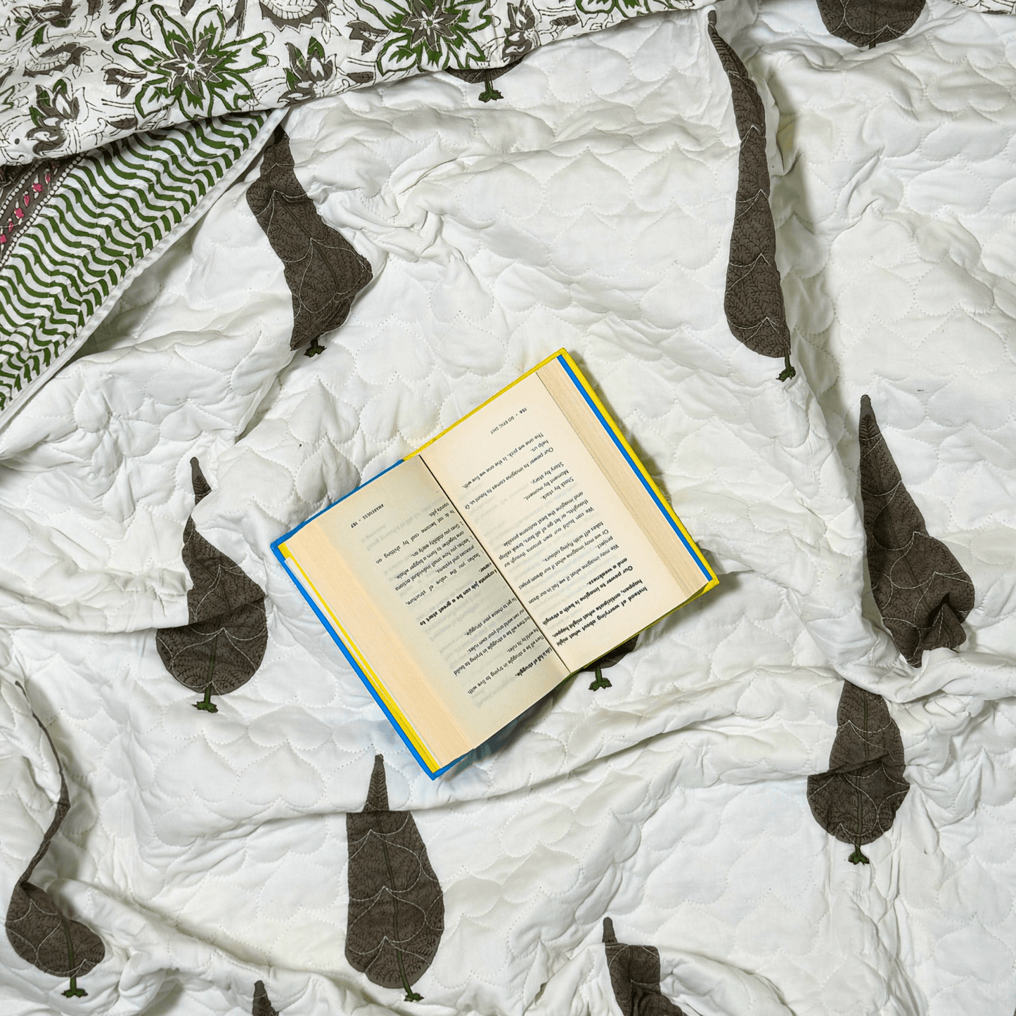 Flat lay of Jaipuri handprinted quilt featuring brown tree motif and open book for cozy styling