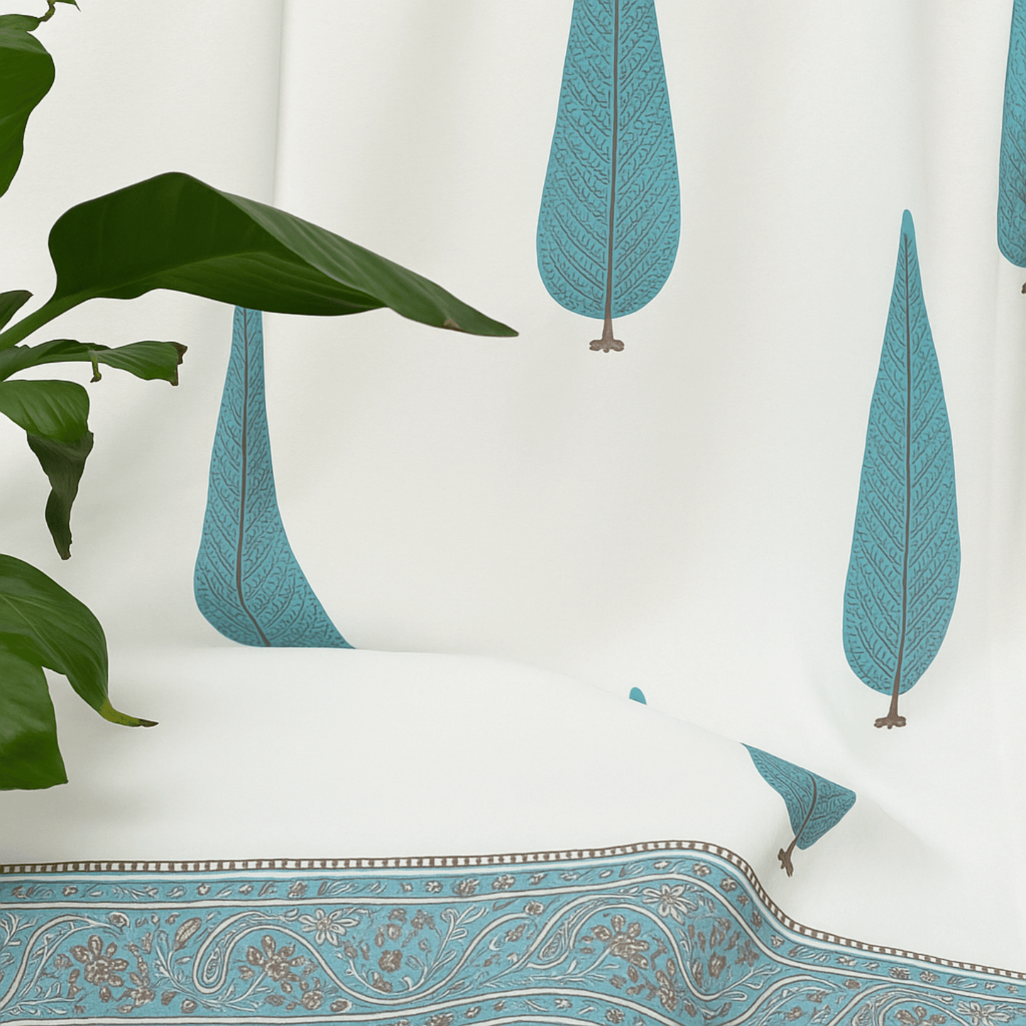 Side view of cotton curtain with blue tree block print, styled beside a leafy green indoor plant