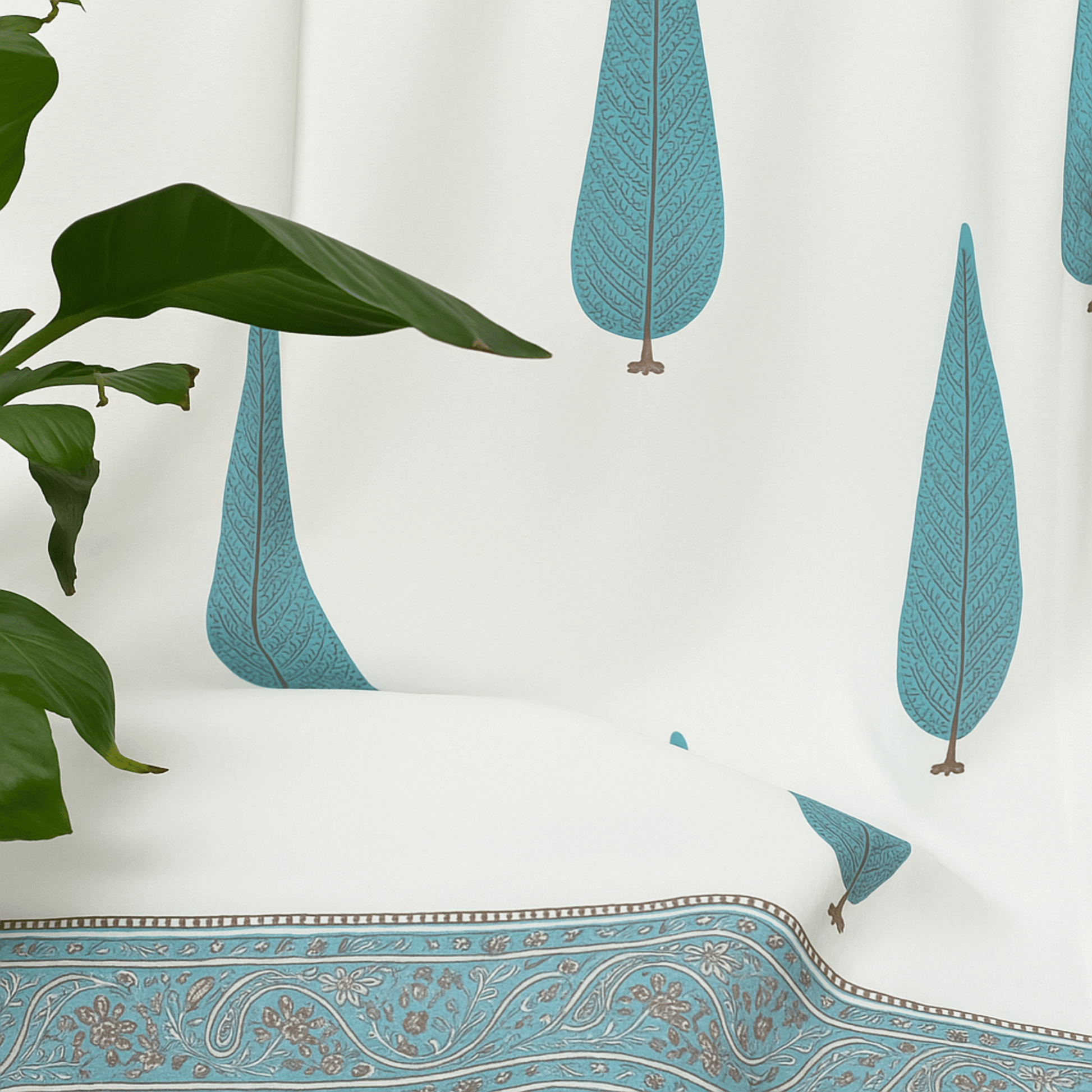 Side view of cotton curtain with blue tree block print, styled beside a leafy green indoor plant