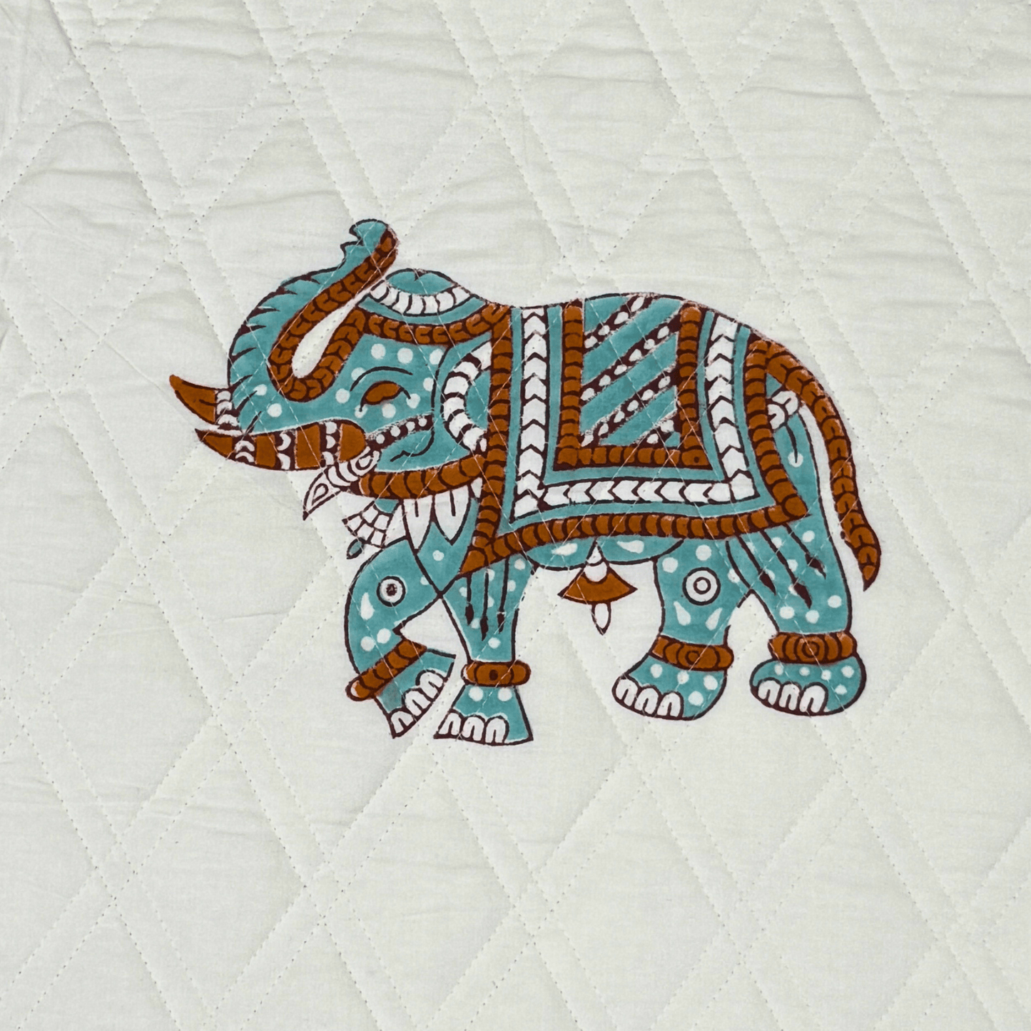 Close-up of a single elephant block print on white quilted fabric, handprinted in earthy tones with fine detailing.

