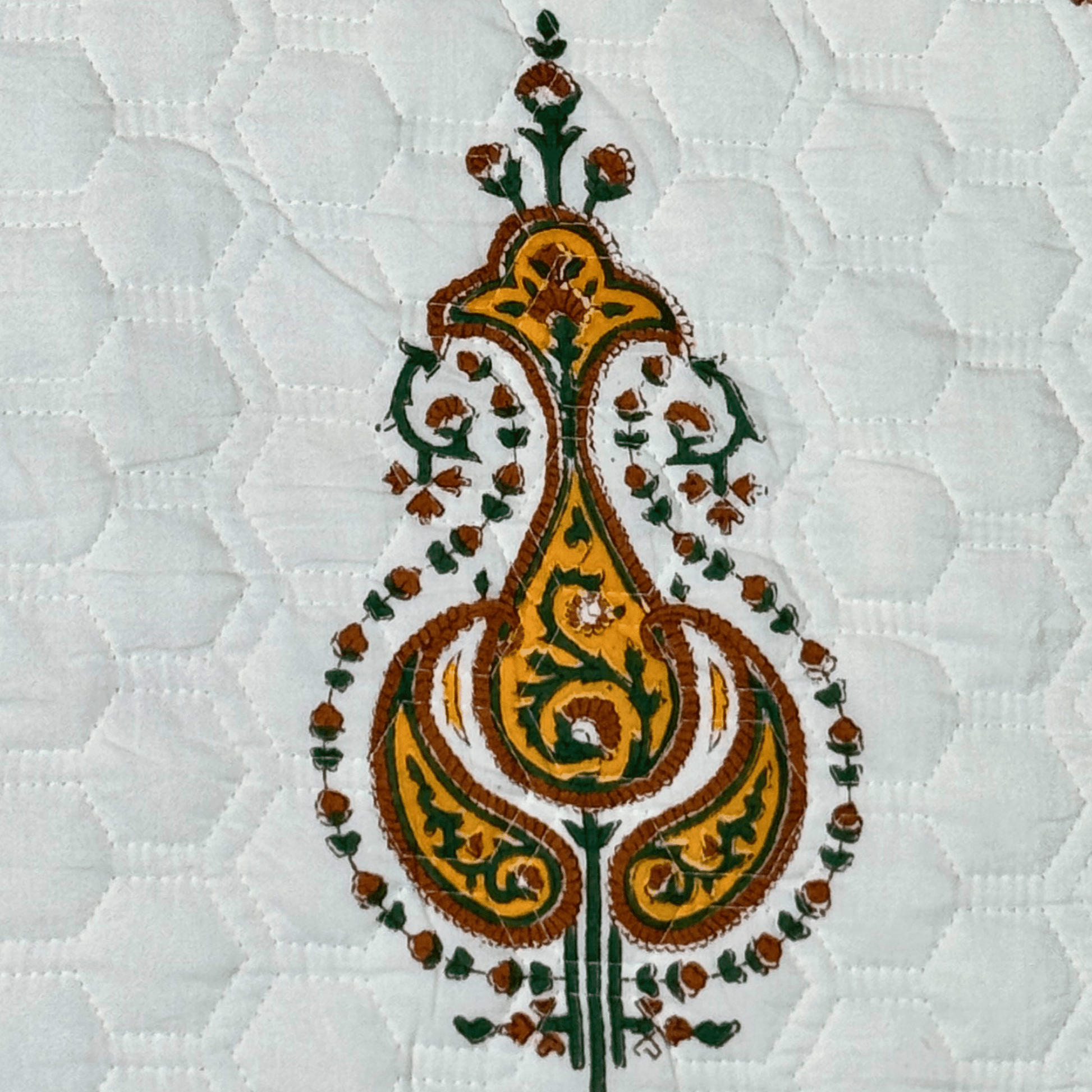Close-up of a single yellow and green paisley motif on a white hand-quilted cotton base with honeycomb stitching.
