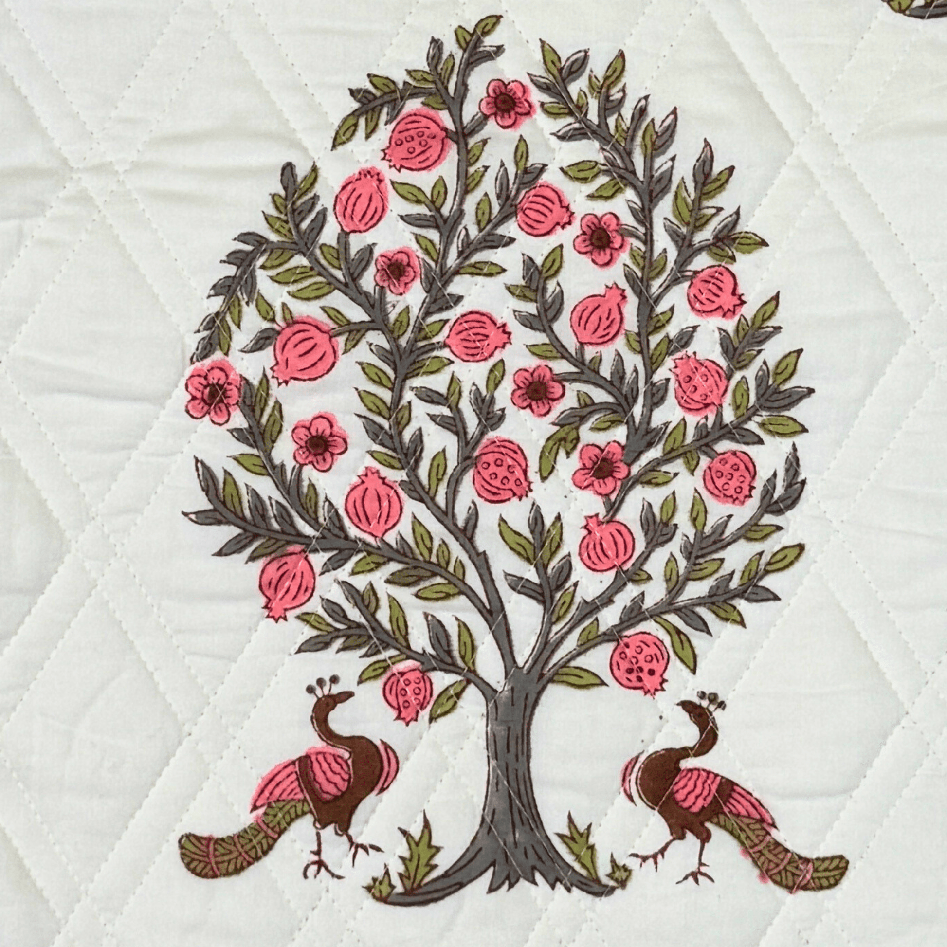 Detailed view of handprinted quilt featuring twin peacocks under a pomegranate tree with pink floral accents