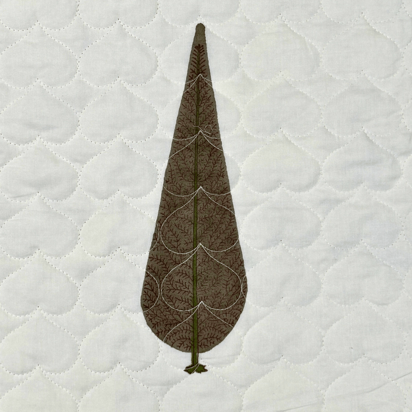 Detailed view of handblock printed brown cypress tree on scallop-stitched white cotton quilt