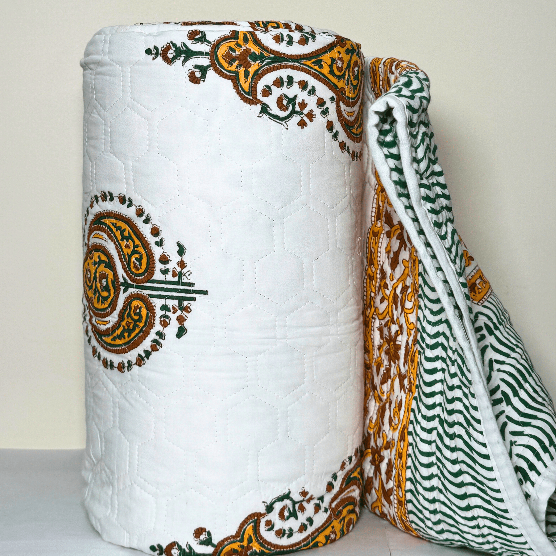 Rolled Jaipuri quilt with detailed paisley block prints and floral borders, showing both the printed front and striped reverse side.