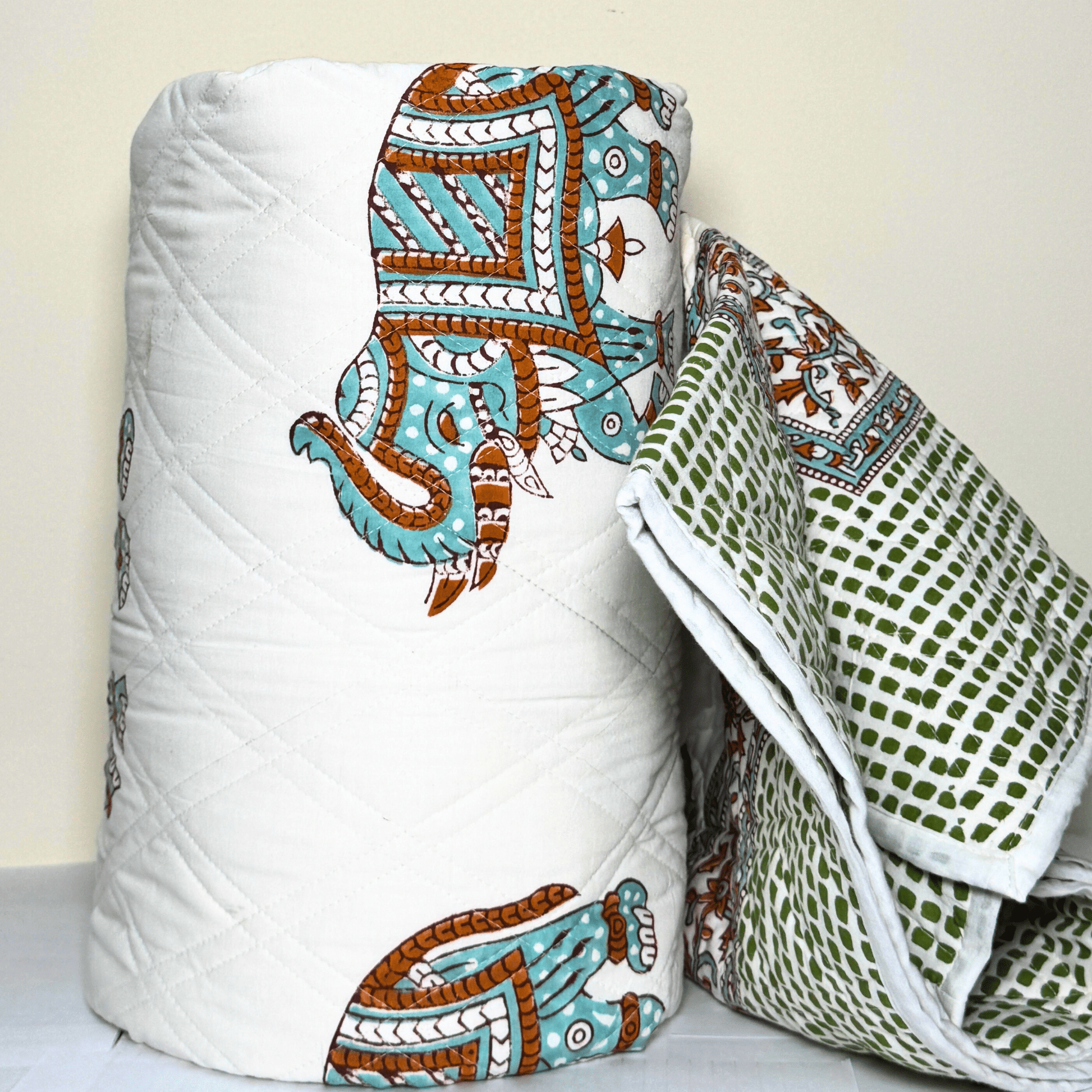 Rolled Jaipuri cotton quilt with turquoise elephant motif and green dotted back, showcasing reversible traditional design.
