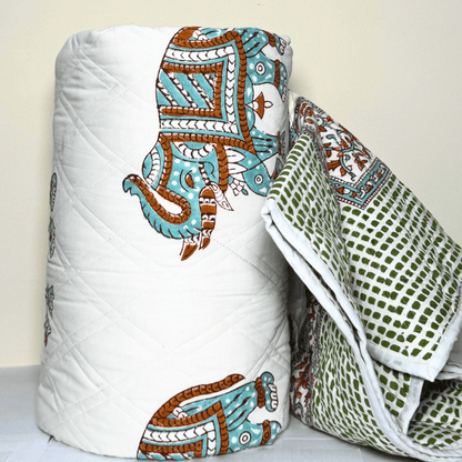 Rolled Jaipuri cotton quilt with turquoise elephant motif and green dotted back, showcasing reversible traditional design.